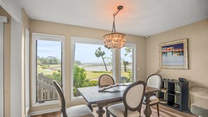Comedor con mesa y sillas de madera, ventanas amplias con vistas a un campo de golf y una araña.