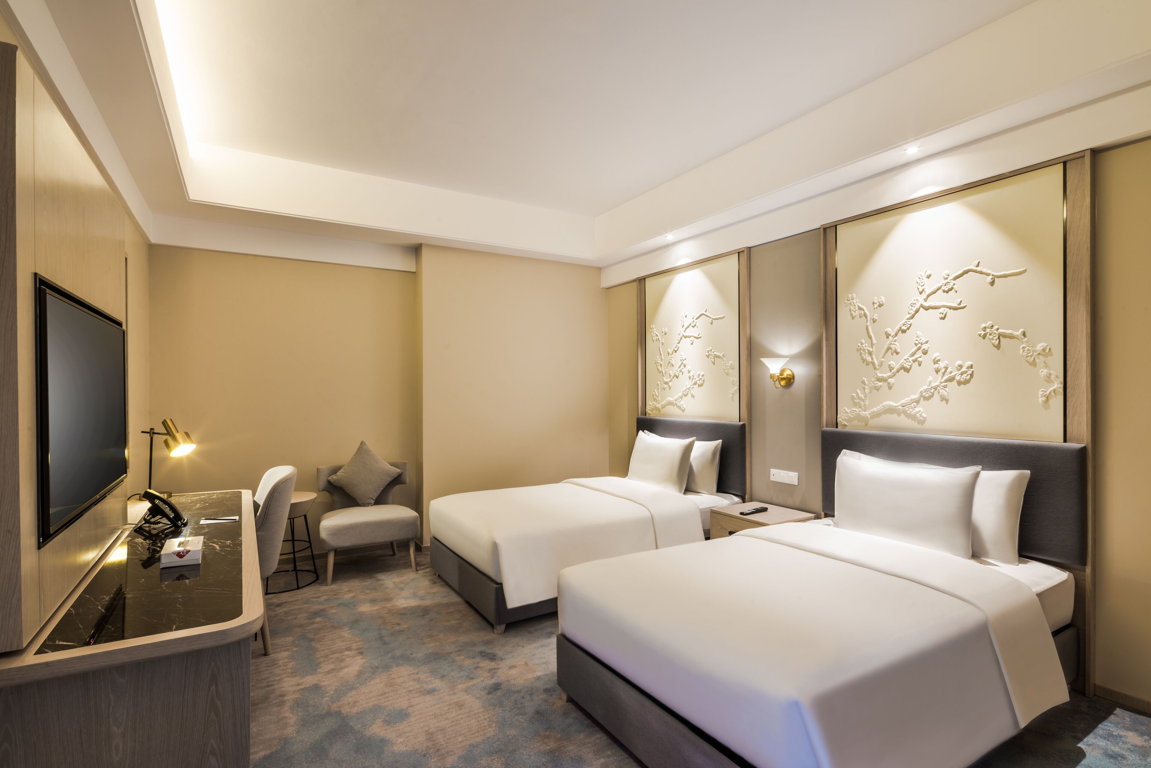 A hotel room with two beds, a desk, a chair, and a TV.