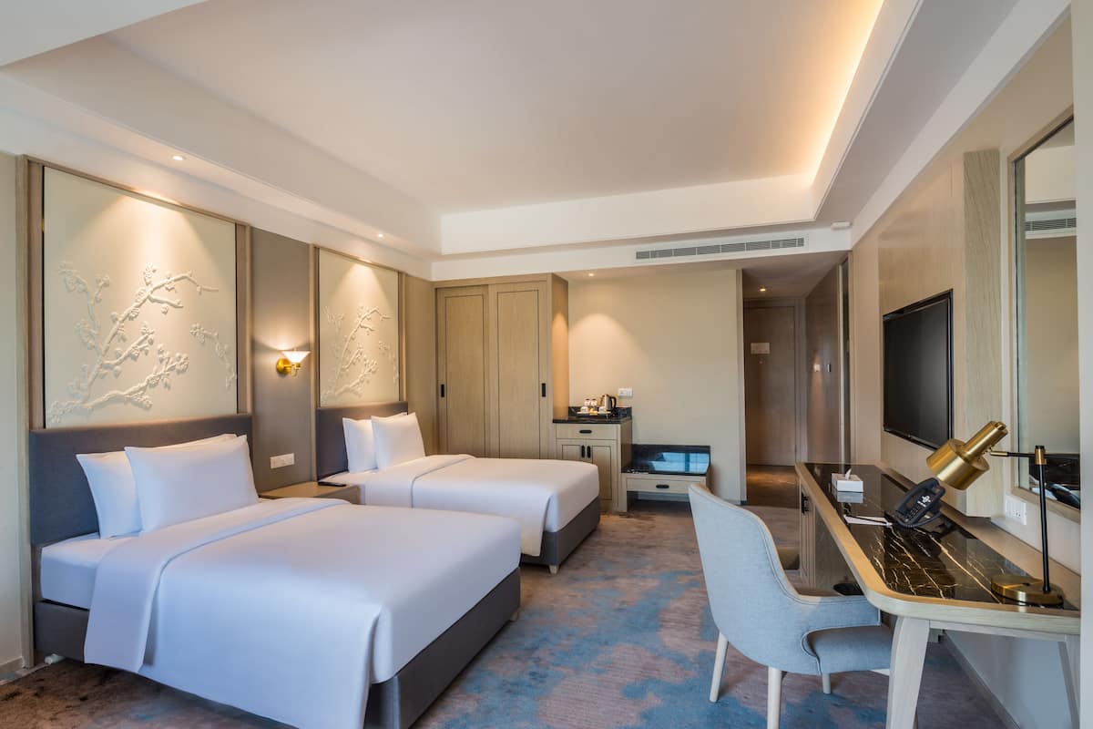 A hotel room with two beds, a desk with a chair, a TV, and a minibar.