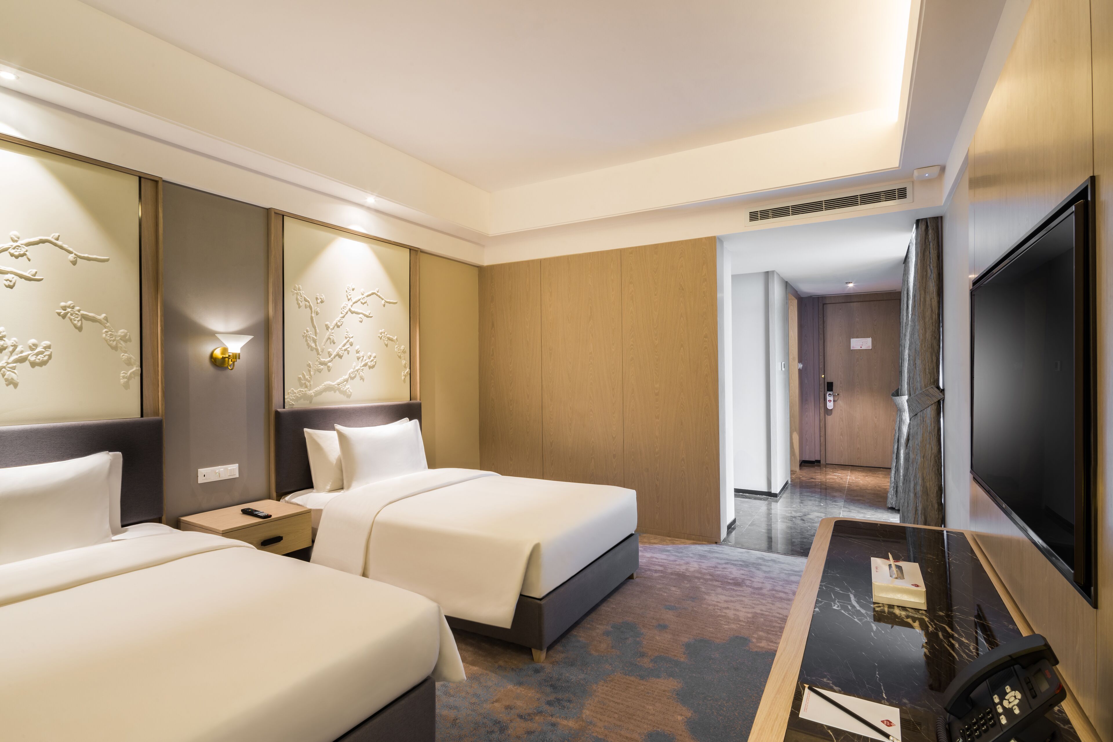 Une chambre d’hôtel avec deux lits, un bureau, un téléviseur à écran plat et une lampe fixée au mur.