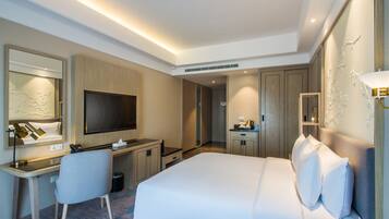 Una habitación de hotel moderna con una cama grande, un escritorio con silla, un televisor y una mesita de noche con lámpara.