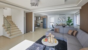 Uma sala de estar ampla com um sofá cinza, uma mesa de centro redonda e uma escada que leva a outro andar.