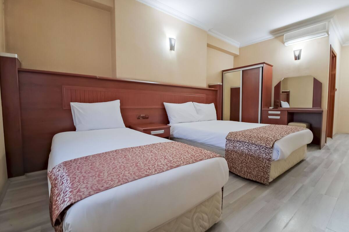 Een hotelkamer met twee bedden, een houten hoofdbord, een bureau met een stoel en een spiegel.