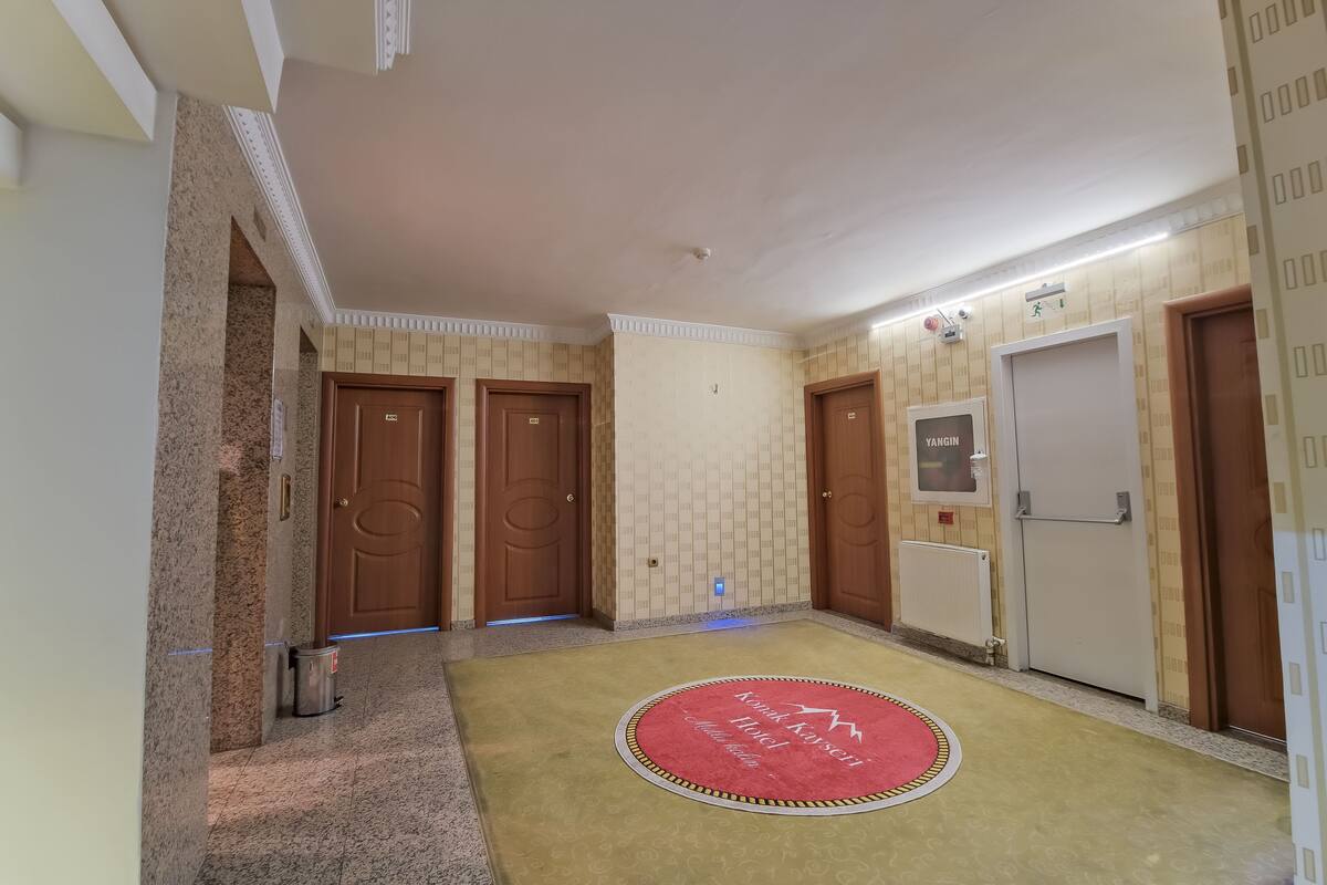 Een hotel lobby met een rood tapijt, meerdere houten deuren en een bord aan de muur.