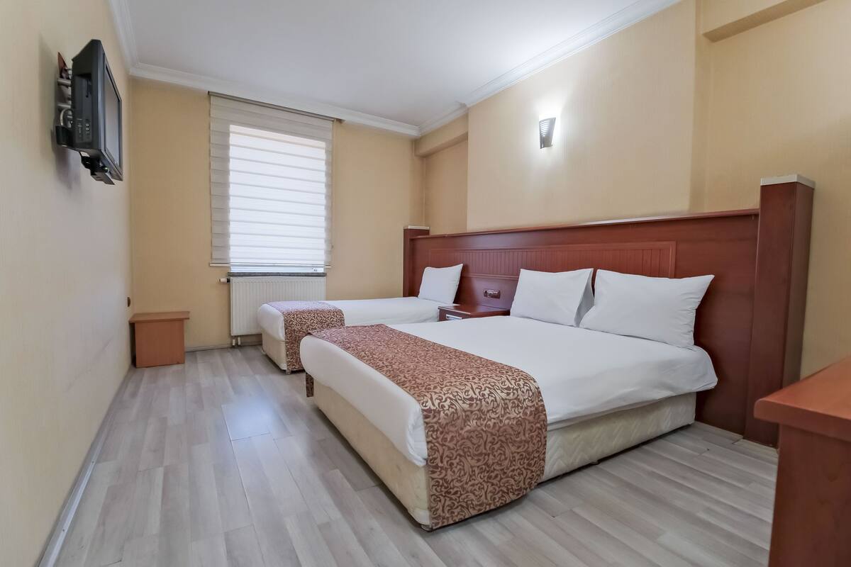 Een hotelkamer met twee bedden, een aan de muur bevestigde televisie, een raam met zonwering en een houten vloer.