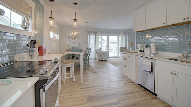 A modern kitchen with white cabinets, a glass backsplash, and a dining area with a table and chairs.