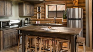 A rustic kitchen with wooden cabinets, a stainless steel refrigerator, and a large island with stools. - Beautiful Log Cabin in Paradise Valley, Montana (Livingston)