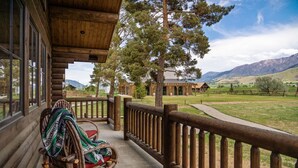 A wooden cabin with a porch, a rocking chair, and a view of a mountain landscape. - Beautiful Log Cabin in Paradise Valley, Montana (Livingston)