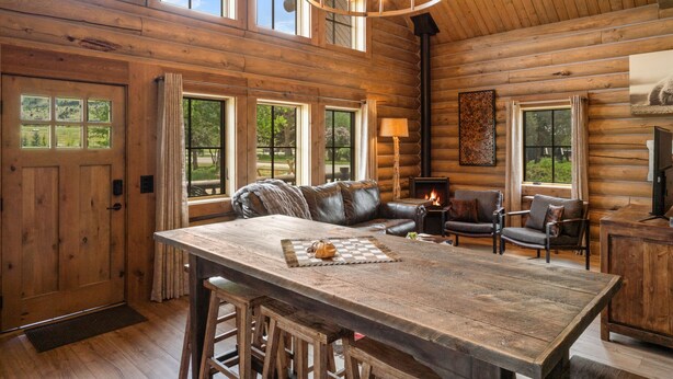 A log cabin interior with a large wooden dining table, leather sofas, and a fireplace. - Beautiful Log Cabin in Paradise Valley, Montana (Livingston)