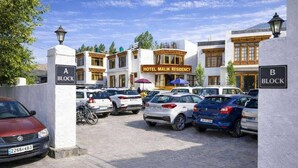 A hotel with a traditional architectural style, featuring a central building labeled "Hotel Malik Residency." There are multiple parked cars in front of the hotel, and a sign indicating "A Block" and "B Block" for parking areas. - Hotel Malik Residency (Leh)
