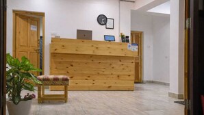 A reception area with a wooden desk, a computer, a clock, and a plant. - Hotel Malik Residency (Leh)