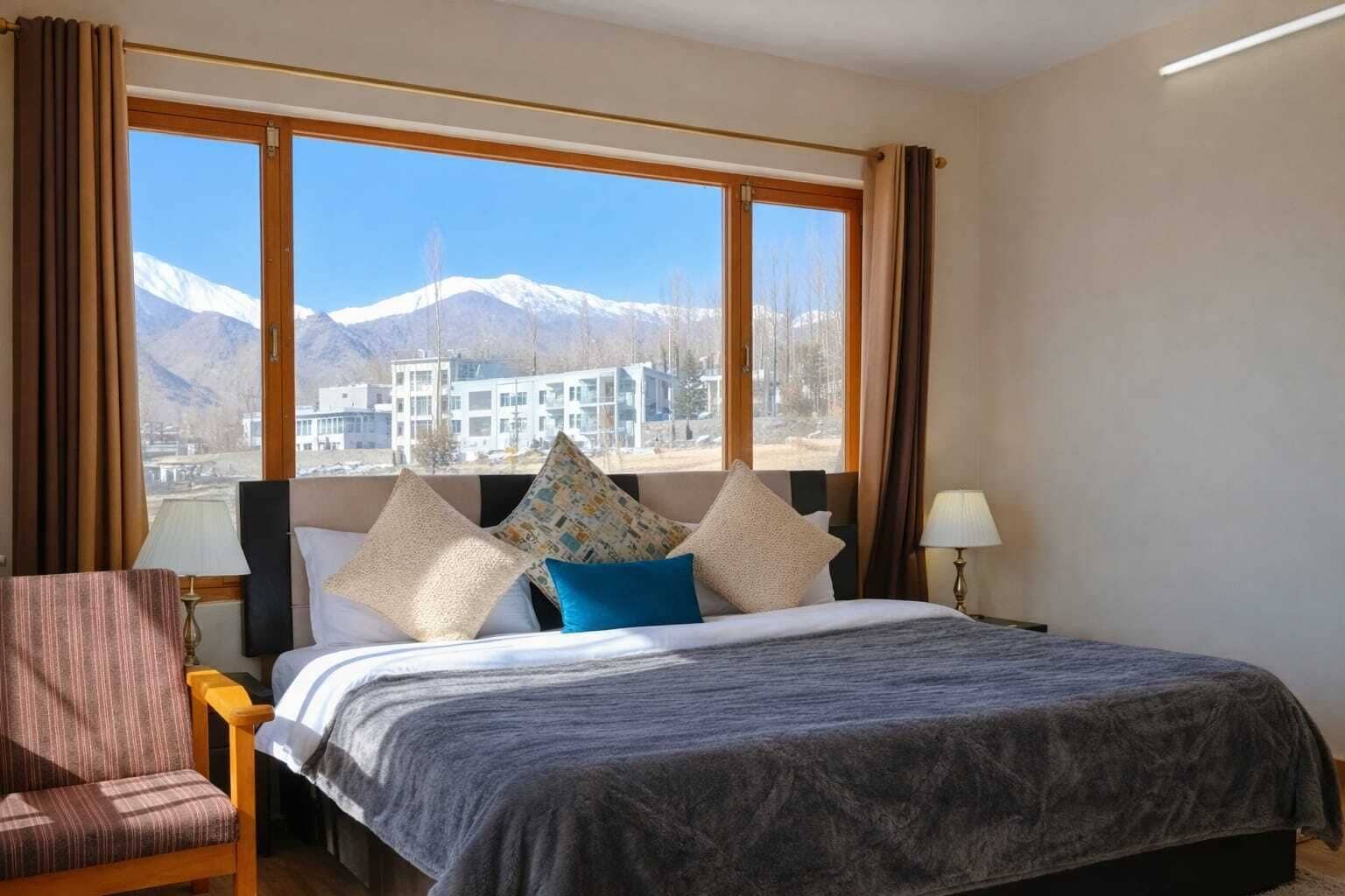 A hotel room with a bed, a chair, a nightstand, and a window with a mountain view.