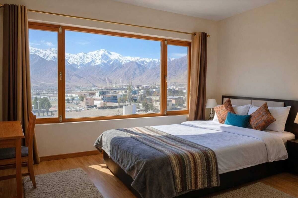 A hotel room with a large window offering a mountain view, a bed with pillows, and a wooden chair.