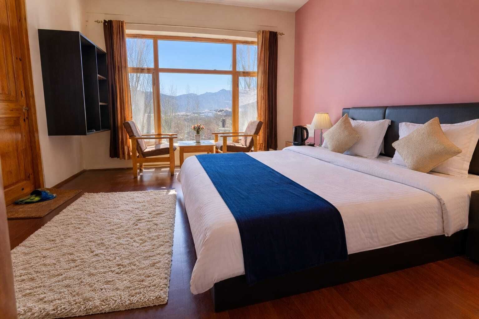 Una camera d'hotel con un letto grande, una scrivania, due sedie, una TV e una finestra vista montagne.