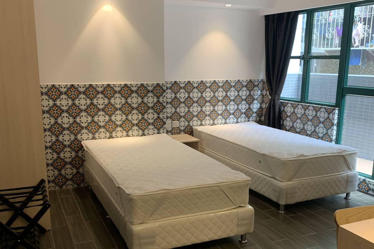 A room with two beds, a wooden floor, and a patterned wall.