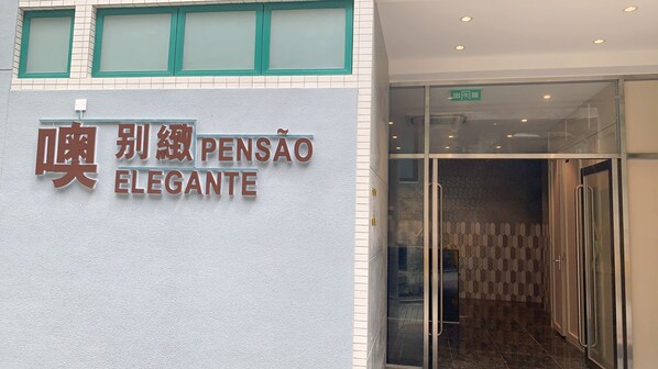 A hotel entrance with a sign reading "PENSÃO ELEGANTE" and a glass door leading inside.