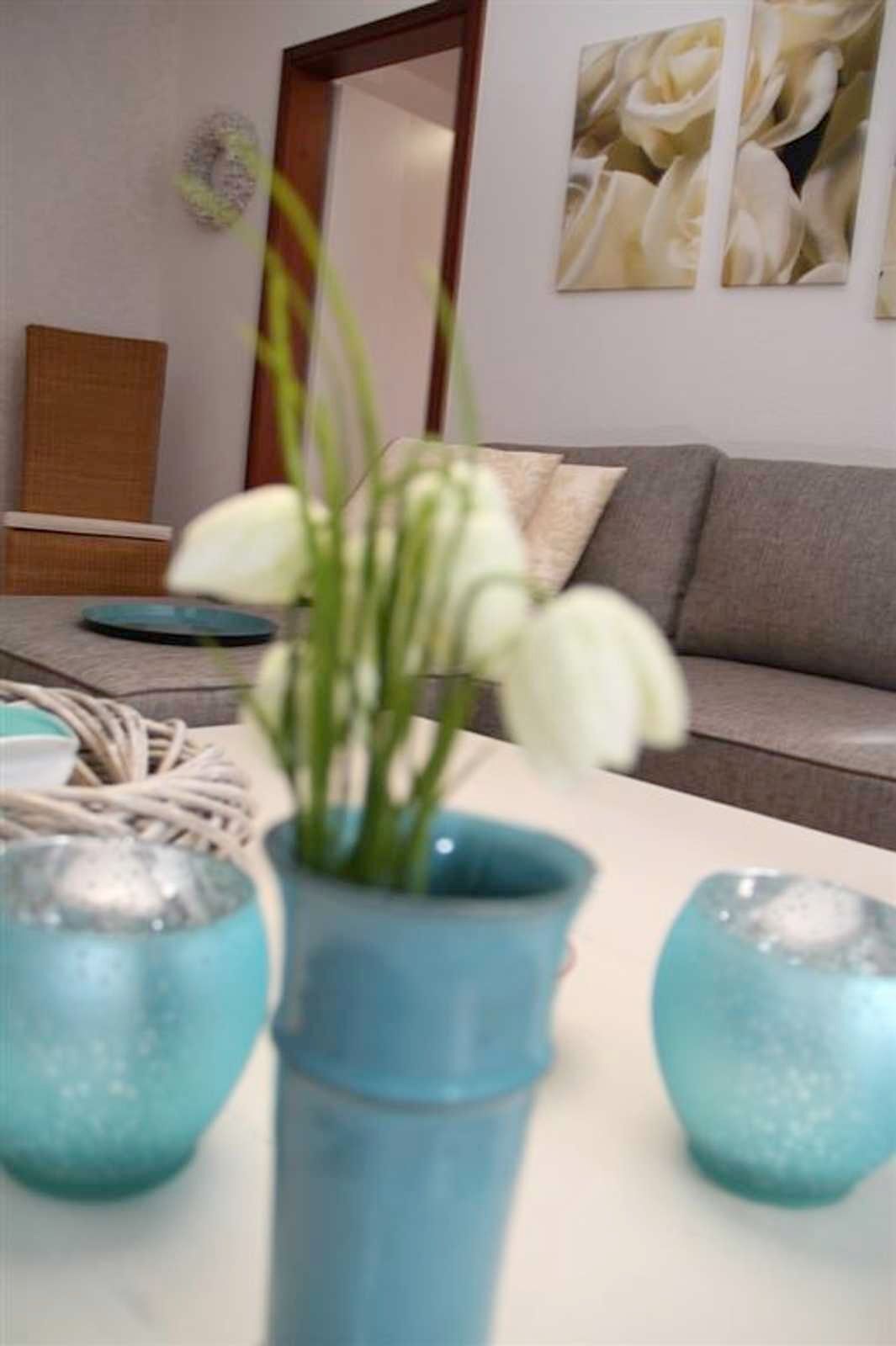 A living room with a sofa, a coffee table, and a vase with white flowers.