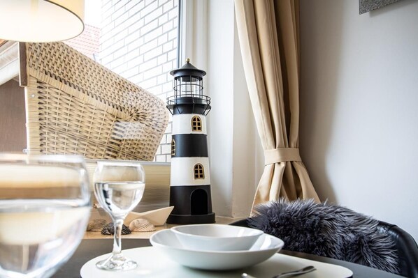 A room with a table set for dining, a decorative lighthouse, a wicker basket, and a fur throw on a chair.