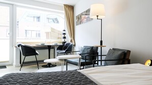 A hotel room with a bed, a desk with a chair, a sofa, and a lamp.