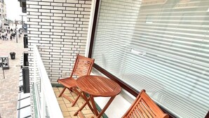 A balcony with wooden chairs and a table, a brick wall, and a large window with blinds.