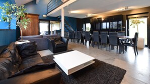 Amplia sala de estar con techo alto, una escalera y un comedor con múltiples sillas y mesas.