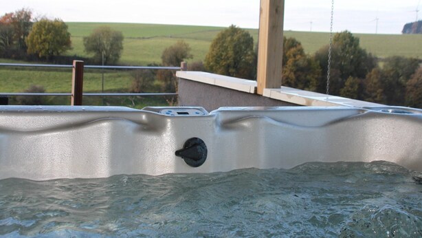 Un jacuzzi con vistas a un paisaje verde y aerogeneradores a lo lejos.
