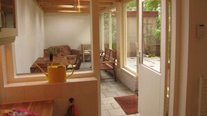 A room with a wooden ceiling, a sofa, a chair, and a window overlooking a garden. - Charming Home by the Lake (West-Grafdijk)