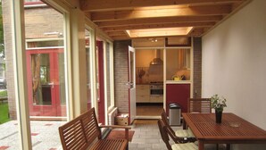 A patio area with wooden furniture, a table, and chairs. There is a view of a kitchen through an open door. - Charming Home by the Lake (West-Grafdijk)