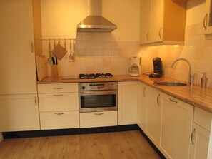Een keuken met witte kasten, een gasfornuis, een oven, een koffiezetapparaat en een spoelbak.