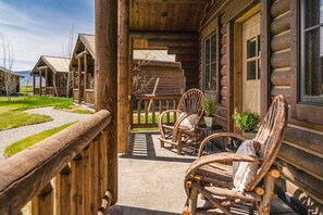 A wooden cabin with a porch, two wicker chairs, and a small table.