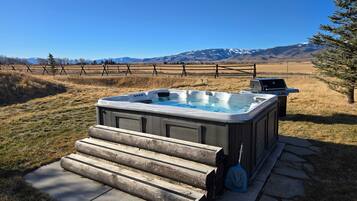 A hot tub with steps leading up to it, a grill, and a view of mountains in the background.