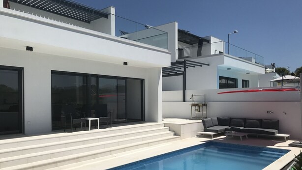 Ett modernt hus med en swimmingpool, en täckt uteplats och en trappa som leder upp till en balkong.