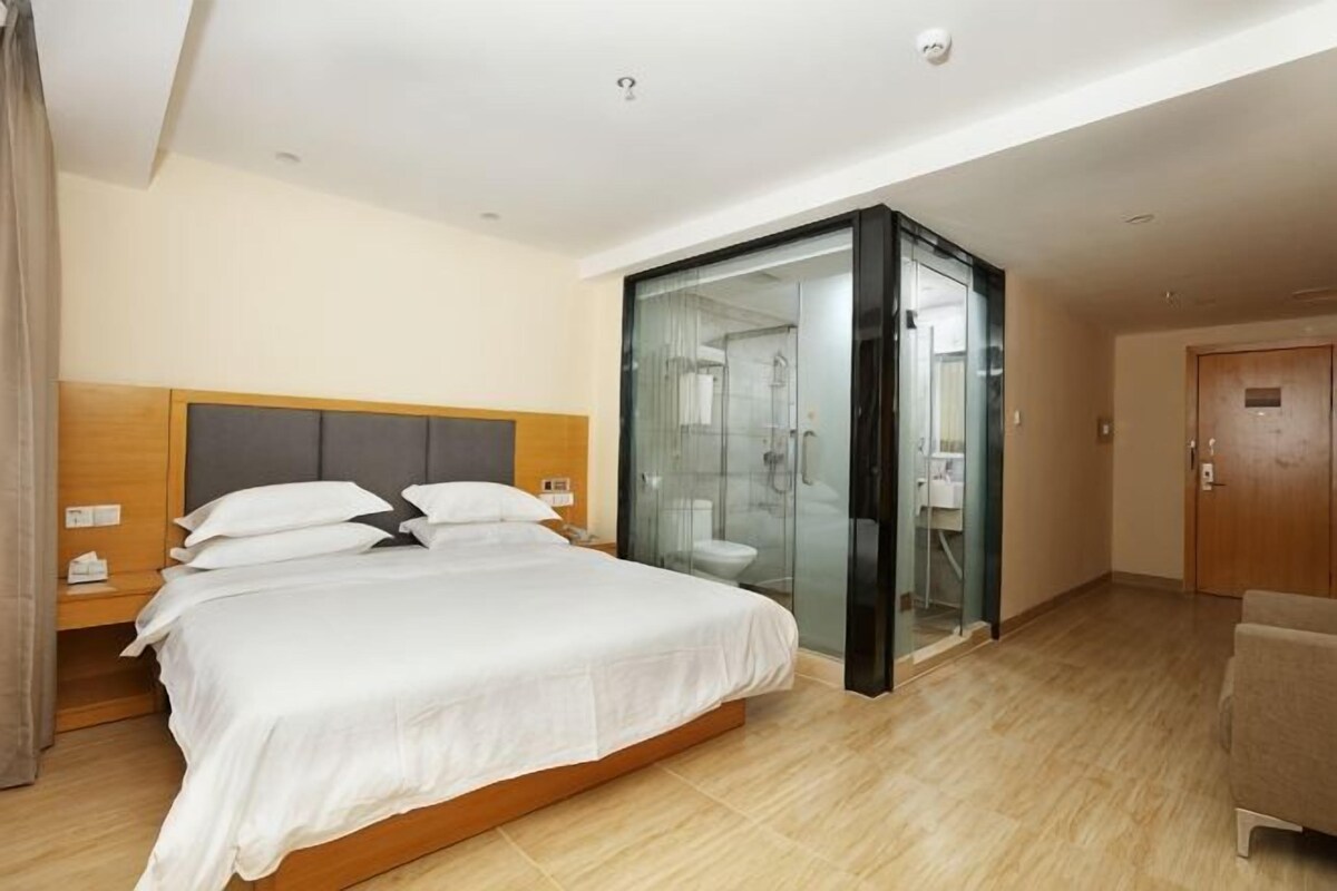 A hotel room with a large bed, a glass-enclosed shower area, and a wooden door.
