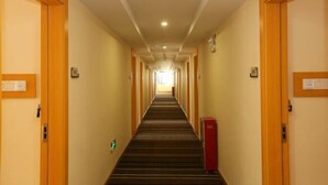 A hotel hallway with carpeted floors, wooden doors on either side, and a red fire alarm box on the right.