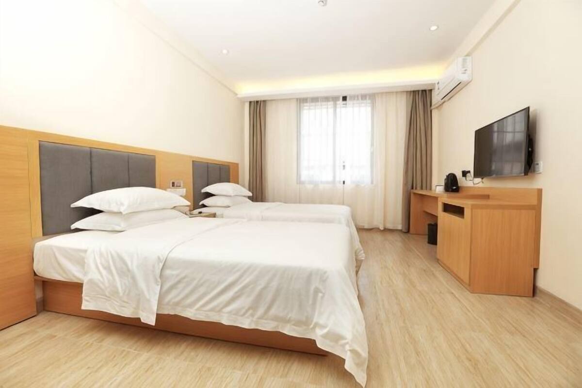 A hotel room with two beds, a desk, a television, and a window with curtains.