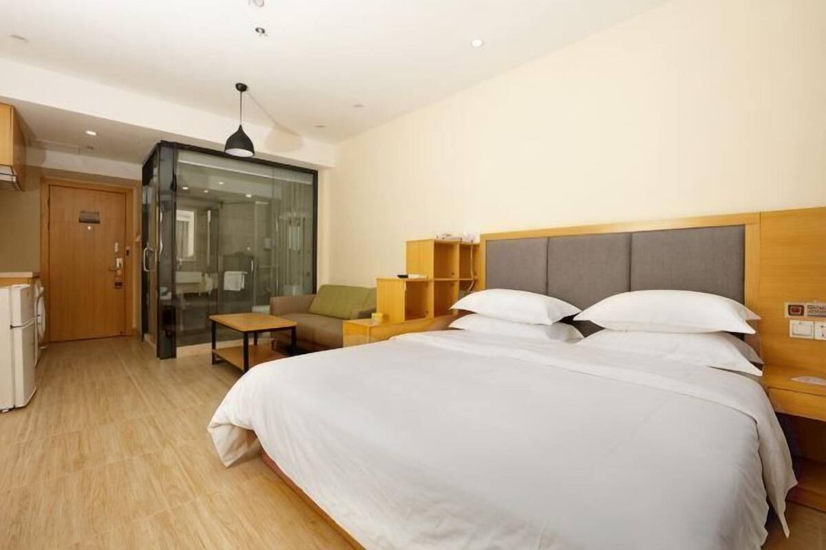 A hotel room with a bed, a desk, a chair, a glass partition, and a wardrobe.