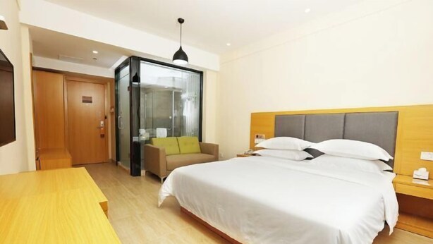 A modern hotel room with a large bed, a wooden desk, a glass partition, and a sofa.