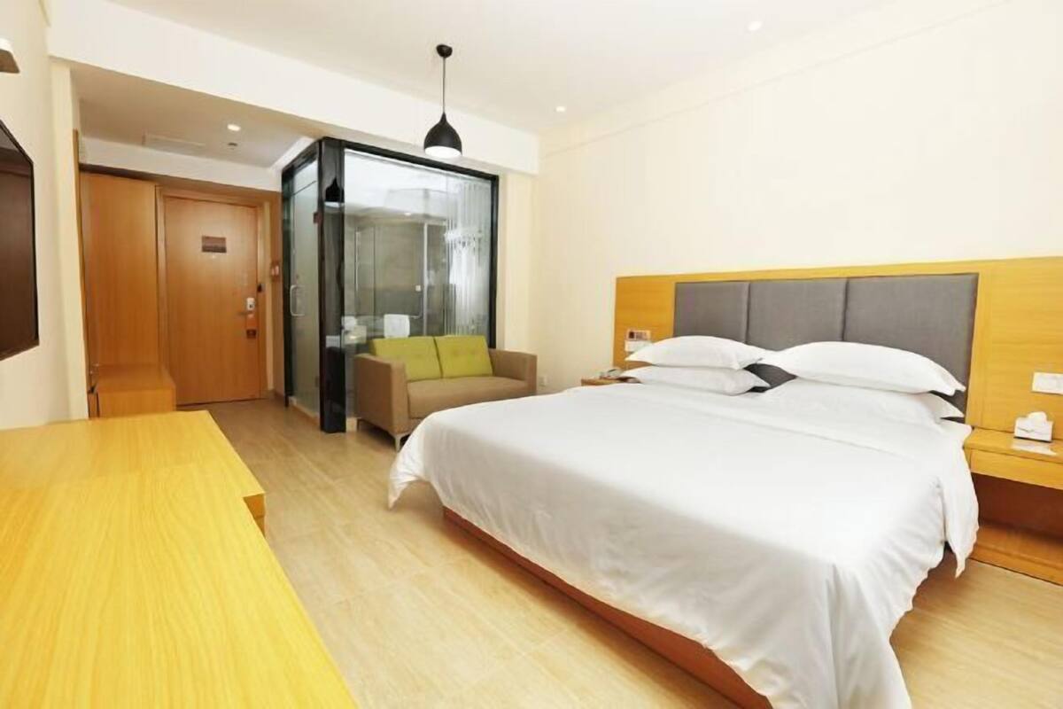 A modern hotel room with a large bed, a wooden desk, a glass partition, and a sofa.