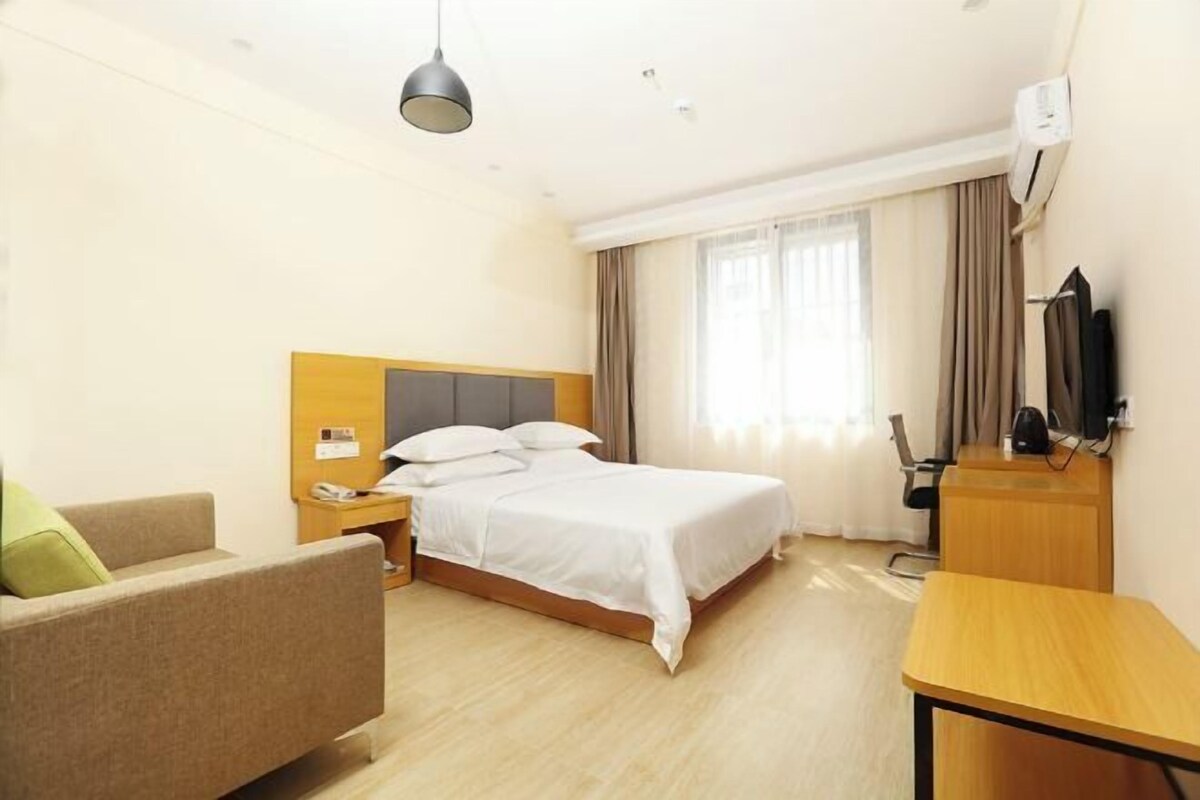 A hotel room with a bed, a desk, a chair, and a television.