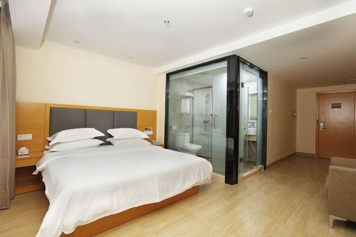 A hotel room with a bed, bedside table, and a glass-enclosed shower area.