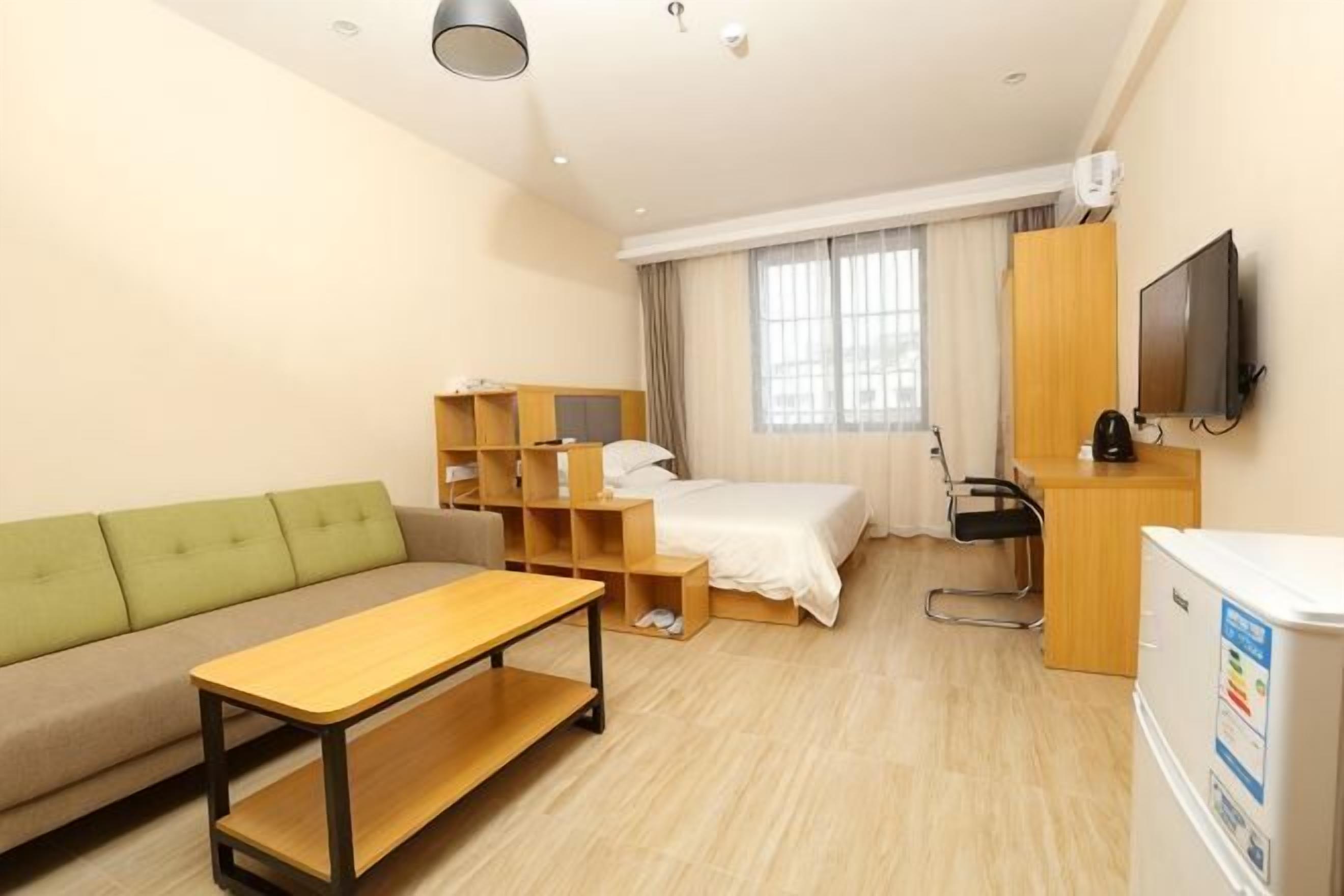 Una habitación de hotel con cama, sofá verde, escritorio, televisor y refrigerador.