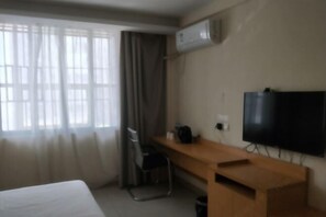 A hotel room with a bed, a desk, a chair, an air conditioner, and a TV mounted on the wall.