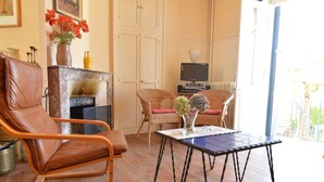 Ein gemütliches Wohnzimmer mit Ledersessel, Korbsessel, einem kleinen Tisch mit einer Vase und einem Kamin.