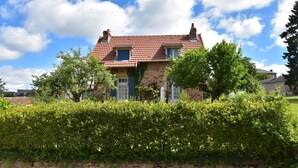 Ein zweistöckiges Steinhaus mit rotem Ziegeldach, umgeben von üppigen Grünhecken und Bäumen.