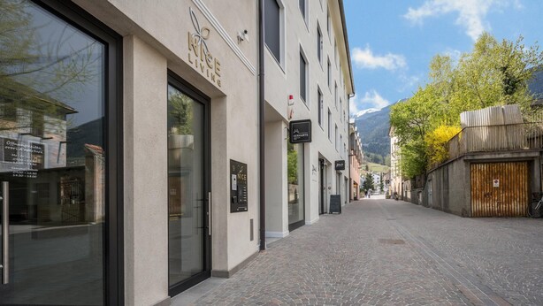 Een geplaveid straatje met een gebouw met grote glasramen en een bord waarop 'RICE LIVING' staat.