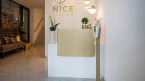 Een receptiebalie met een 'NICE LIVING' bord, een trap, een bank en potplanten.