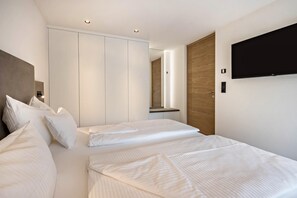 A modern hotel room with a large bed, a TV mounted on the wall, and a wardrobe.