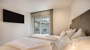 A hotel room with a large bed, a smaller bed, a TV mounted on the wall, and a balcony with chairs. - Modern Apartment "Nice 4" with Balcony in the Center of Bressanone/Brixen (Brixen)