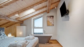 A bedroom with a large bed, a bathtub, a TV, and a window.