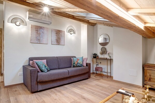 A living room with a sofa, wall-mounted lights, a wooden ceiling, and a small table with a remote control.